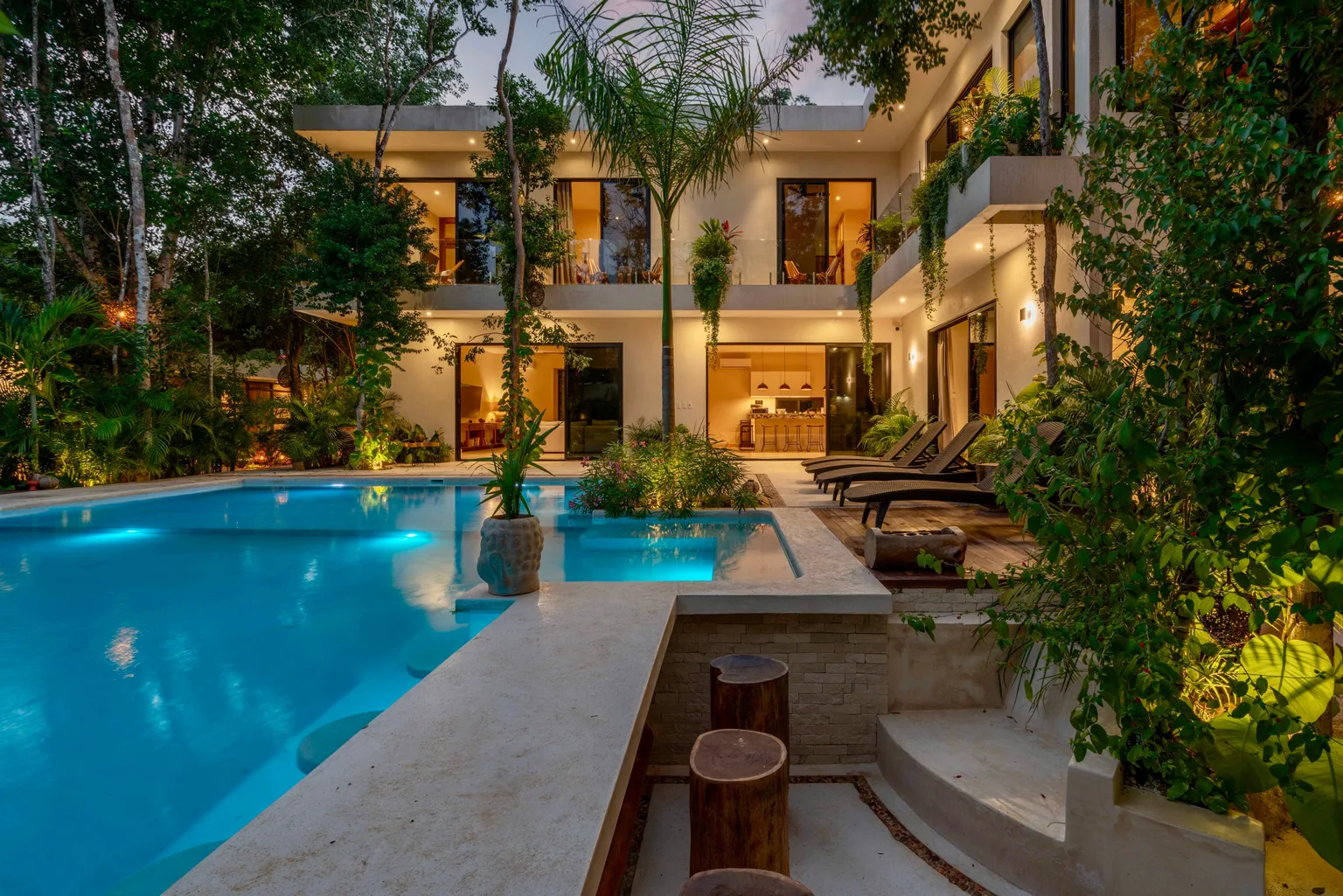 Referência ilustrativa: arquitetura contemporânea com piscina e vegetação tropical ao entardecer.
